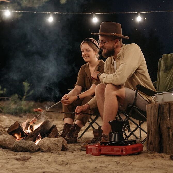 Un cuplu in jurul unui foc, cu echipamentele de camping potrivite pentru a se bucura de natură